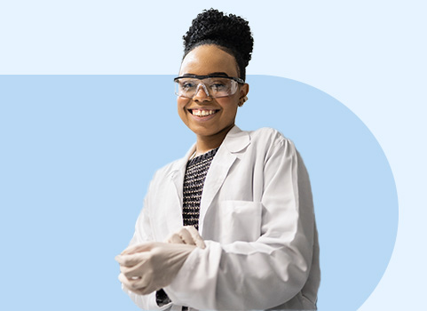 Smiling woman in white lab coat and safety goggles.