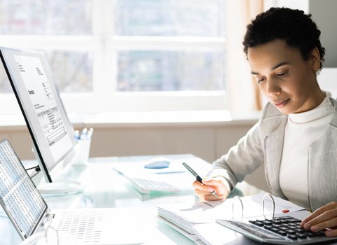 A person with dark skin and dark hair wears a suit and uses a calculator