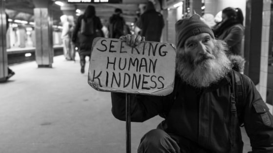 man with sign that says seeking human kindness in subway