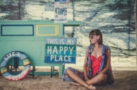 girl on beach sitting next to sign.