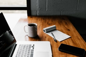desk with a laptop, cellphone, notepad & coffee mug