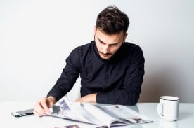 man reading newspaper on white tabletop