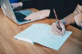 person writing in notebook next to friend