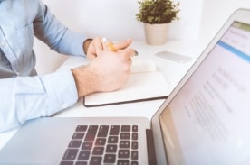 person taking notes with open laptop.