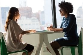 two women chatting at a table.