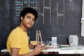 Boy studying by chalkboard wall.