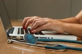 person using laptop next to stethoscope.