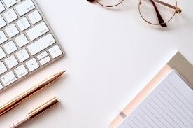 keyboard, notepad, and glasses on white desk.