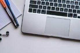 silver laptop and notebook with pens on desk.