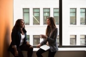 two women talking near window.
