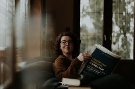 Woman reading newspaper on couch.
