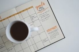 Mug of coffee sitting on open monthly goal planner.