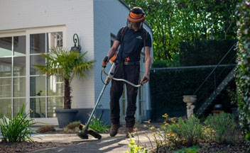 Man standing on sidewalk using weed whacker.