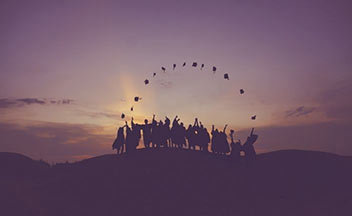 Silhouette of people standing on a hill, throwing graduation caps into the air.