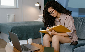 woman writing in notebook sitting on couch.