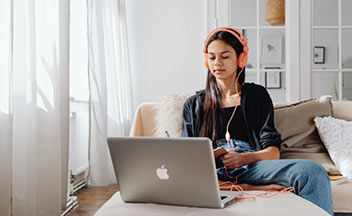 girl with headphones working on Apple laptop.