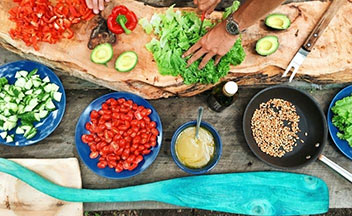 Bowls of colorful food laid out on table while person chops lettuce.