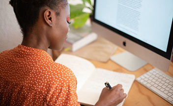 girl taking notes in front of desktop computer.