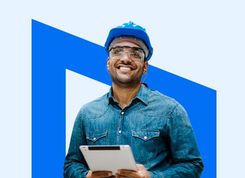 smiling tradesman wearing a hardhat and holding a tablet.