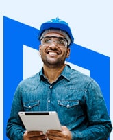 smiling tradesman wearing a hardhat and holding a tablet.