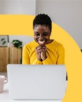 woman in yellow sweater smiling at laptop.