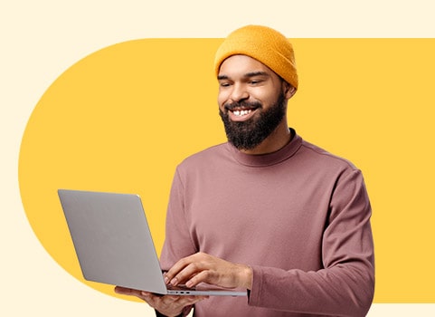 smiling man with beanie holding a laptop.