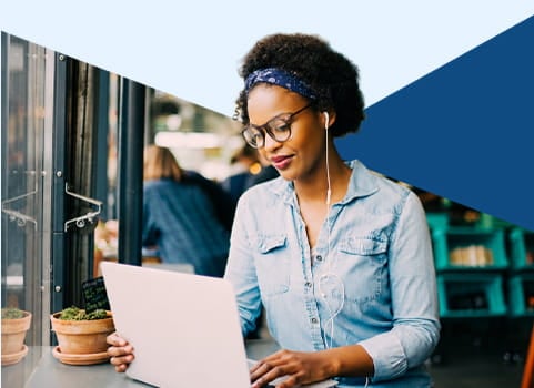 Woman in denim shirt using laptop in a cafe.