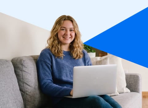 Blonde teen in blue sweater sitting on couch studying on white laptop.