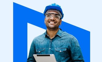 smiling tradesman wearing a hardhat and holding a tablet.