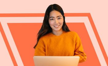 girl in orange sweatshirt with laptop on peach background.