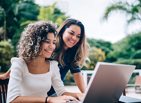 Two woman look at a computer screen, smiling