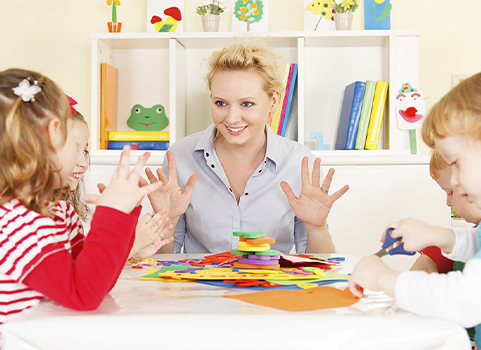 A woman holds up her hands to demonstrate a lesson to four young children