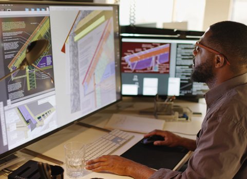 A man with dark skin and dark hair works on a computer