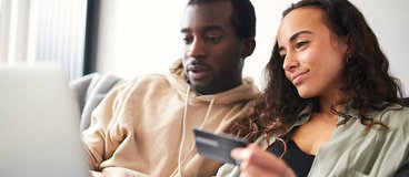 couple sitting together looking at a computer while holding a credit card.