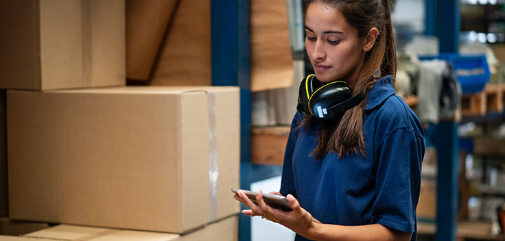 Woman working in a warehouse checking her smartphone.