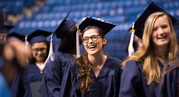Graduates in gowns and graduation caps smiling at the camera.