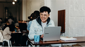 Person sitting in coffee shop with mug and laptop.