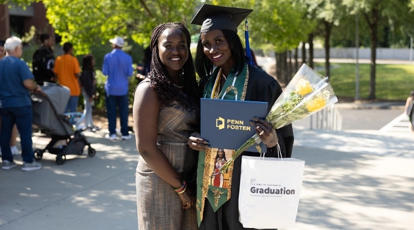 Penn Foster graduate and family member posing with flowers and diploma holder at graduation.