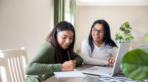 Teen girl and mom sitting together at table studying.