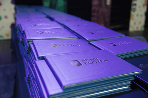 Blue Penn Foster diploma holders stacked on a table.