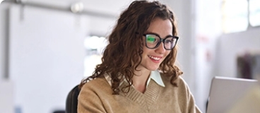 Teen girl with long hair in glasses and beige pullover studying on laptop. 