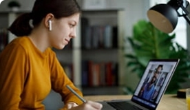 Teen girl in dark yellow shirt with earbuds in watching a video on a laptop.