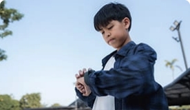 Young teen boy in blue plaid shirt checking watch as he walks outside.