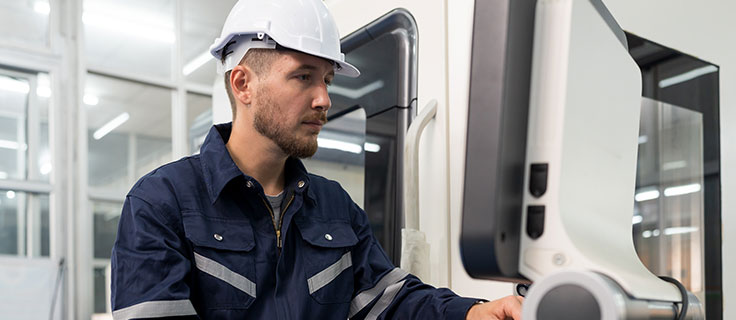 man in white hardhat operating CNC machine.