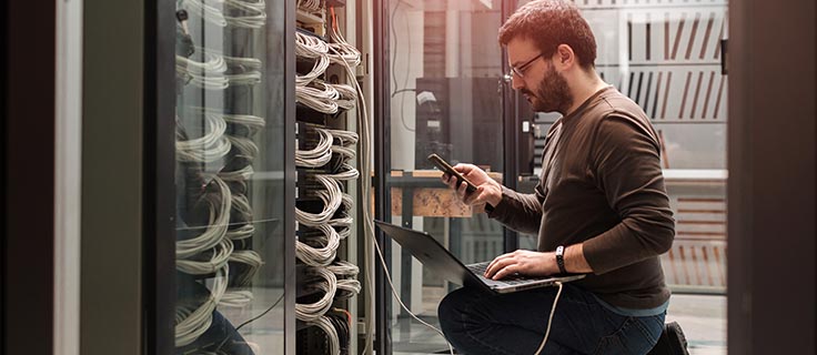 IT technician using laptop in server room.