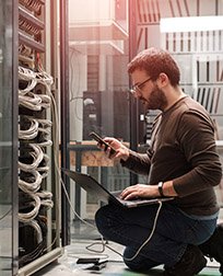 IT technician using laptop in server room.