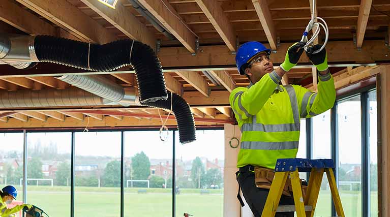 electrician on ladder working on electrical wiring.