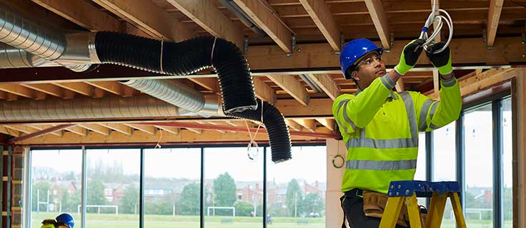 electrician on ladder working on electrical wiring.