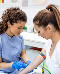 phlebotomist drawing blood from patient in exam room.