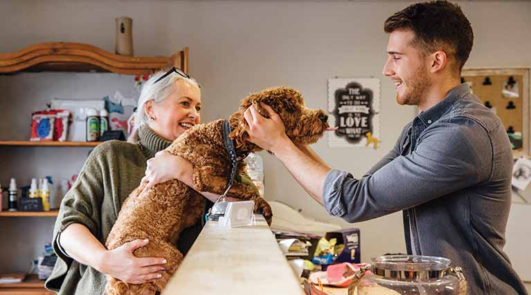 man petting a dog at front desk in a lobby.